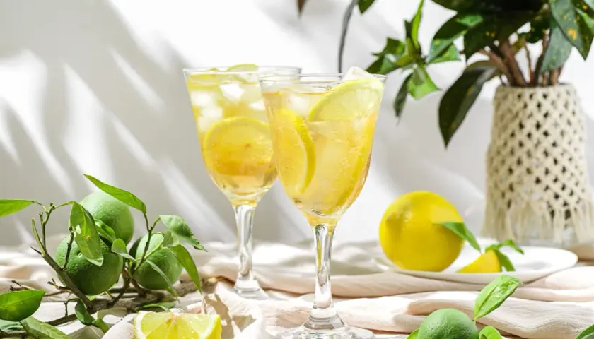 Dwa orzeźwiające drinki z lodem i plasterkami cytryny, idealne na upalne dni. Obok leżą świeże cytryny i zielone owoce.