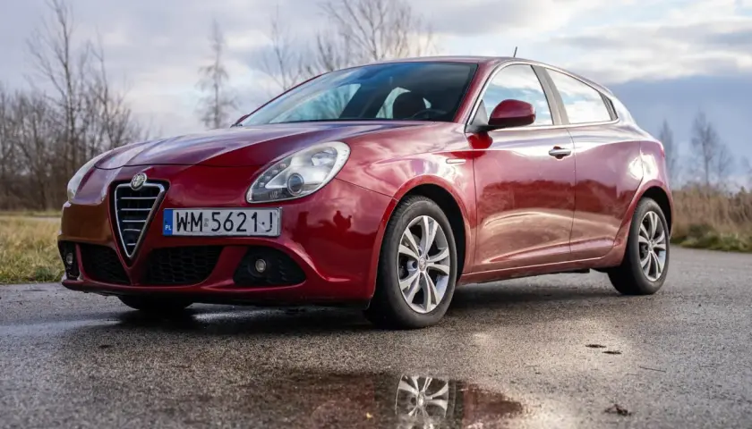 Czerwone Alfa Romeo Giulietta na mokrej drodze. Wiele osób szuka alfa romeo giulietta opinie przed zakupem.