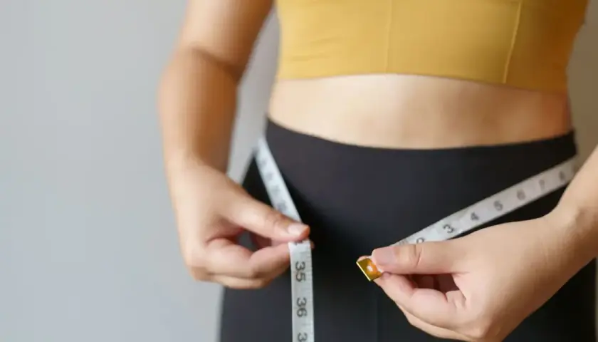 Kobieta mierzy talię centymetrem. Chcesz wiedzieć, jak podkręcić metabolizm po 40.? To pierwszy krok do celu.