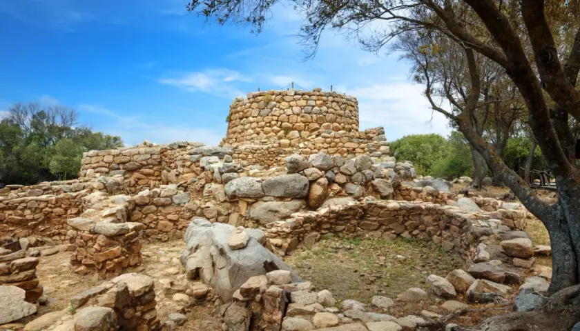Rovine di un nuraghe in pietra sotto un cielo azzurro. Un mistero su chi ha costruito i nuraghi.