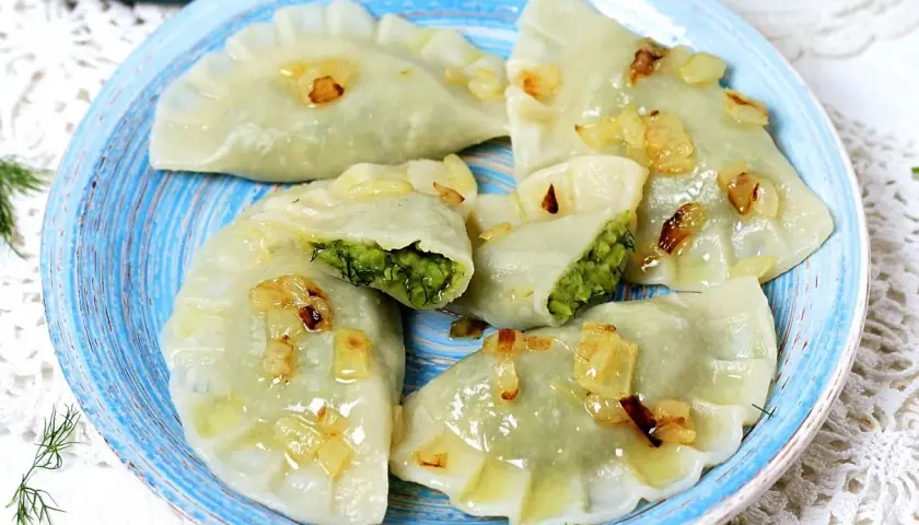 Pyszne pierogi z bobem, polane skwarkami z cebulki, na niebieskim talerzu.