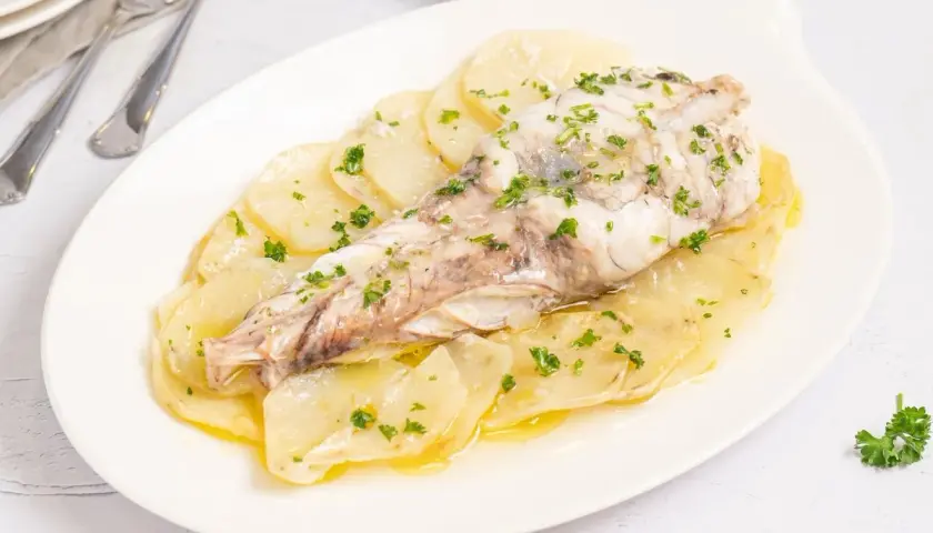 Rape al horno servido sobre patatas laminadas y espolvoreado con perejil fresco.