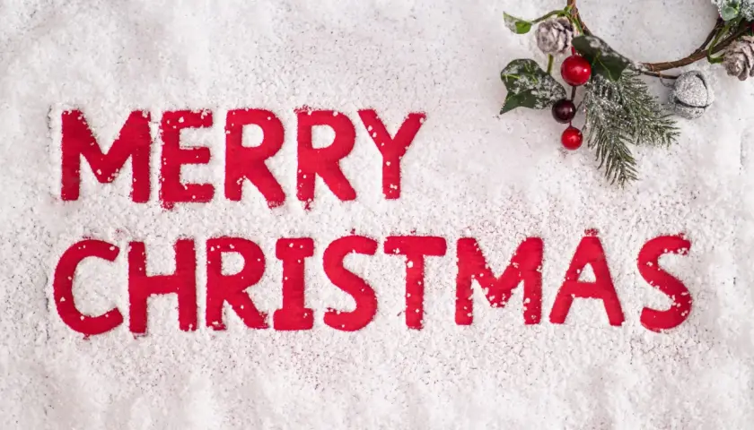 Lettere rosse su neve scrivono "Merry Christmas". Un festoso ramoscello natalizio con bacche e pigne completa la scena, evocando le classiche frasi natalizie in inglese.