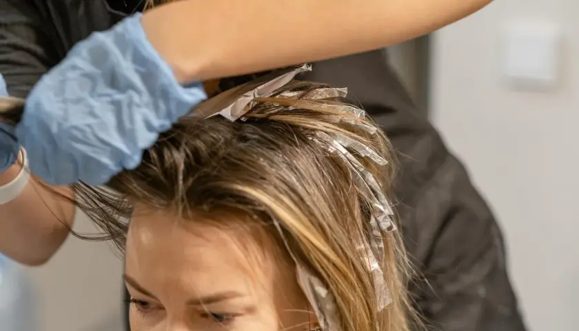 Manos enguantadas aplican mechas con papel de aluminio para un look face framing.