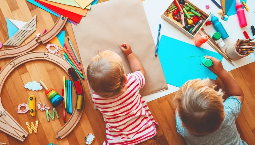 Dos niños pequeños disfrutan de actividades para niños de un año en guardería: pintan y juegan con un tren de madera.