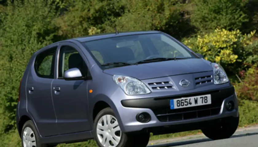 Niebieski Nissan Pixo z tablicą rejestracyjną 8654 W 78 zaparkowany na tle zieleni.