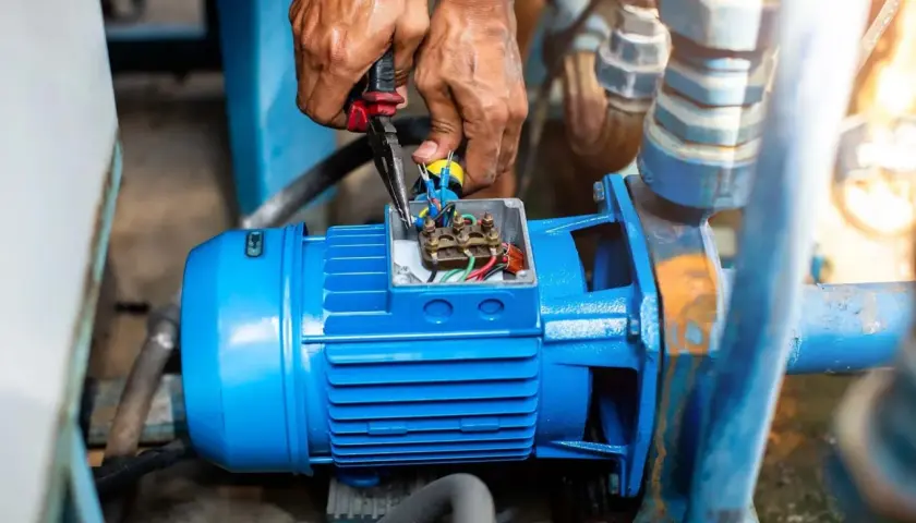 Manos trabajando en la caja de conexiones de un motor azul, revisando el cableado. El **vac significado** es crucial para el funcionamiento de esta bomba.