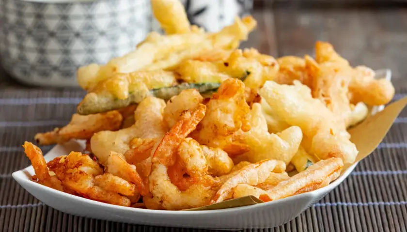 Un piatto invitante di gamberi in tempura dorati e croccanti, accompagnati da verdure fritte.