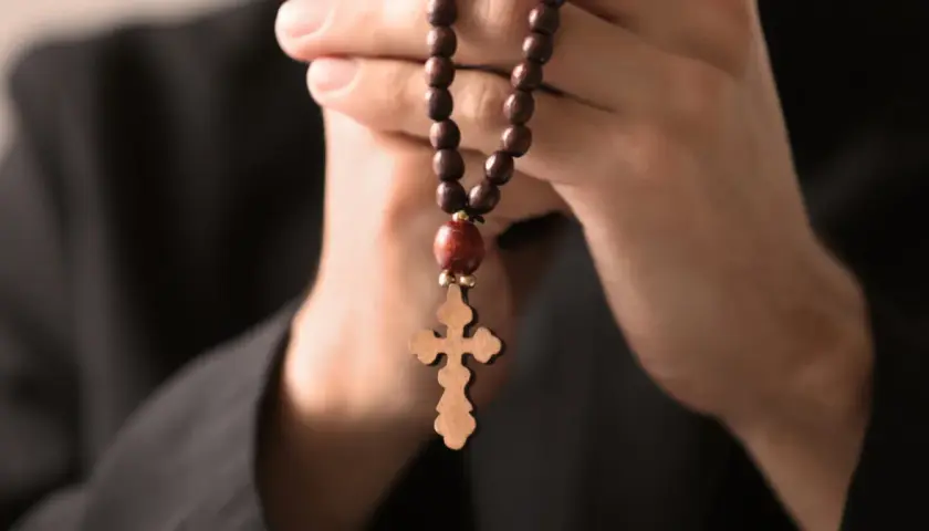Dłonie trzymające drewniany różaniec z krzyżem, symbolizujące modlitwę do archanioła Rafała o uzdrowienie.
