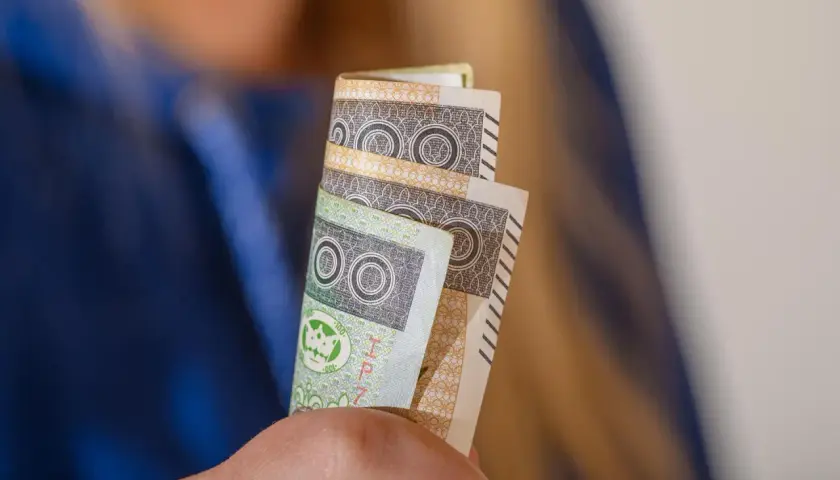 Orzeczenie o niepełnosprawności to podstawa do ubiegania się o zasiłek pielęgnacyjny. Dłonie trzymają banknoty 100 zł.