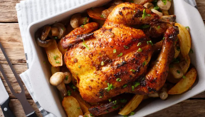 Un délicieux poulet au four, doré et croustillant, servi avec des pommes de terre rôties et des champignons.