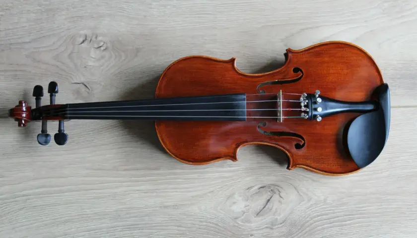 Eleganckie skrzypce leżą na drewnianym blacie. To instrument, który pozwala grać pierwsze skrzypce w orkiestrze, symbolizując lidera i główną melodię.