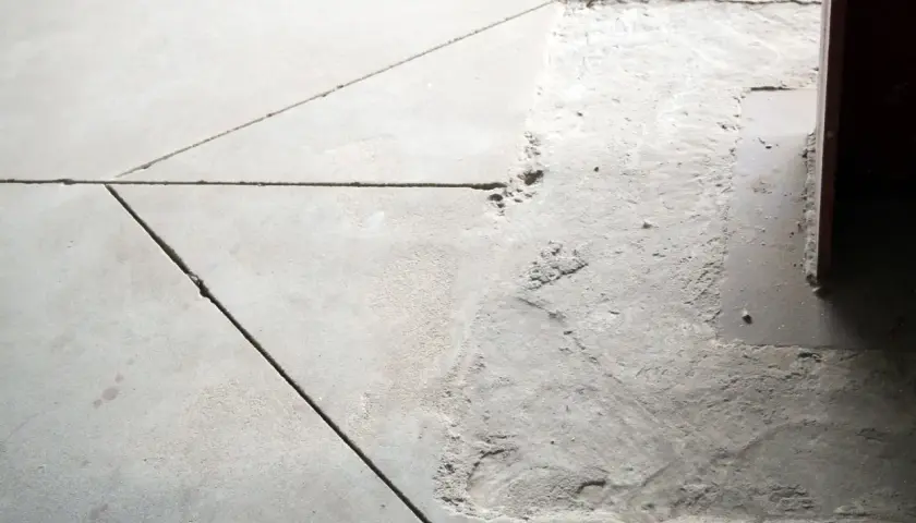 Szara posadzka z widocznymi fugami i ubytkiem betonu. Dylatacja co to? To przerwa między elementami, zapobiegająca pękaniu.