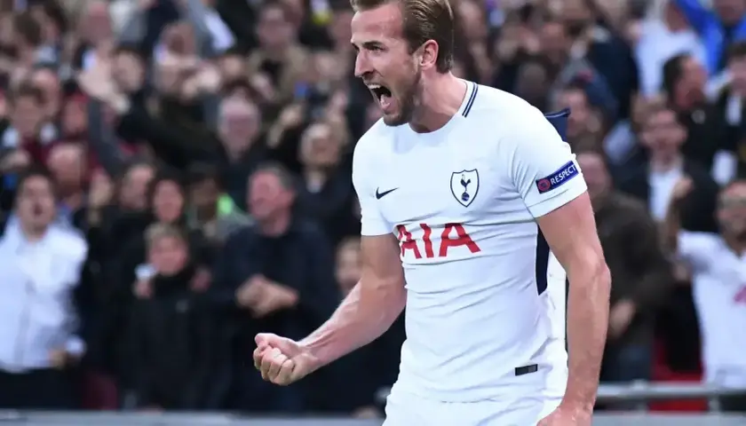 Harry Kane, jeden z najlepszych angielskich trenerów, świętuje bramkę. Tłum kibiców na trybunach.