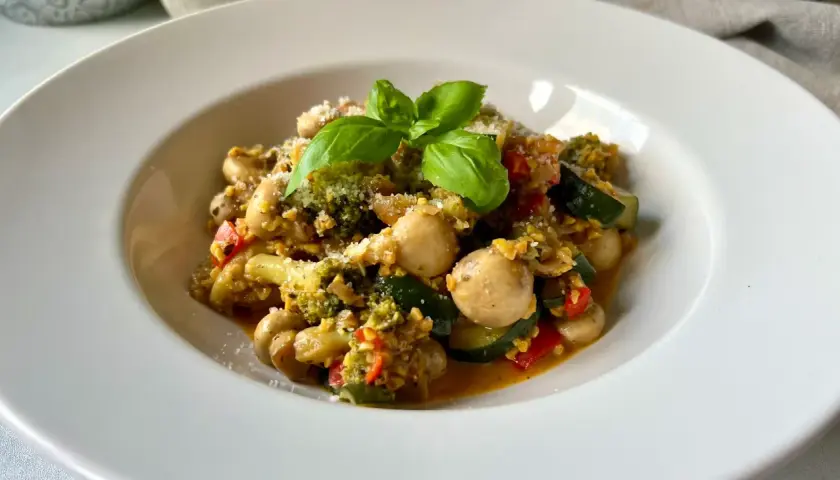 Pyszne kaszotto z warzywami: brokuły, cukinia, pieczarki i pomidorki, posypane parmezanem i udekorowane bazylią.