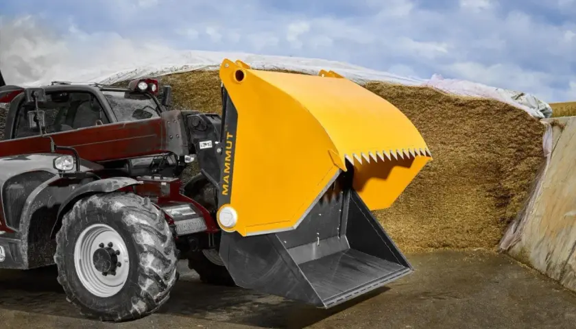 Ein Teleskoplader mit gelber Schaufel steht vor einem großen Silo in der Landwirtschaft.