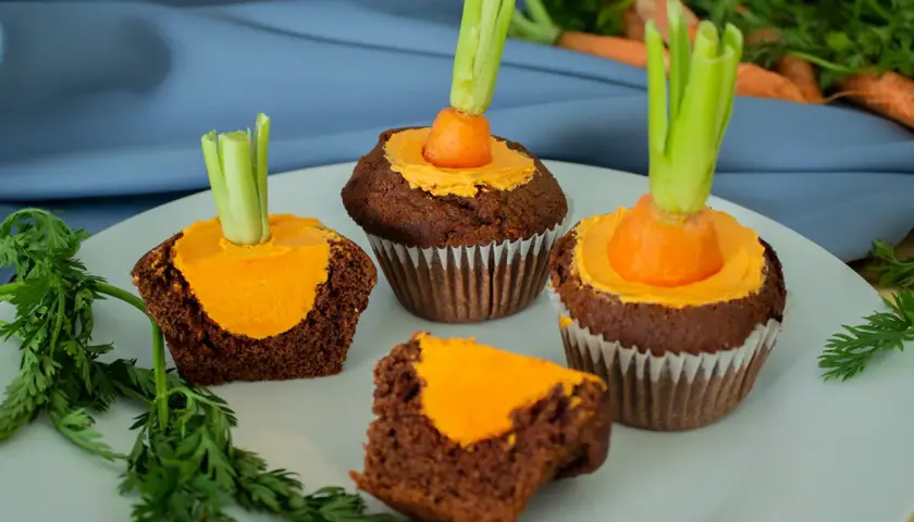 Schokoladen-Muffins mit orangefarbener Glasur und einem kleinen Karottenstück mit Grün als Osterdekoration.