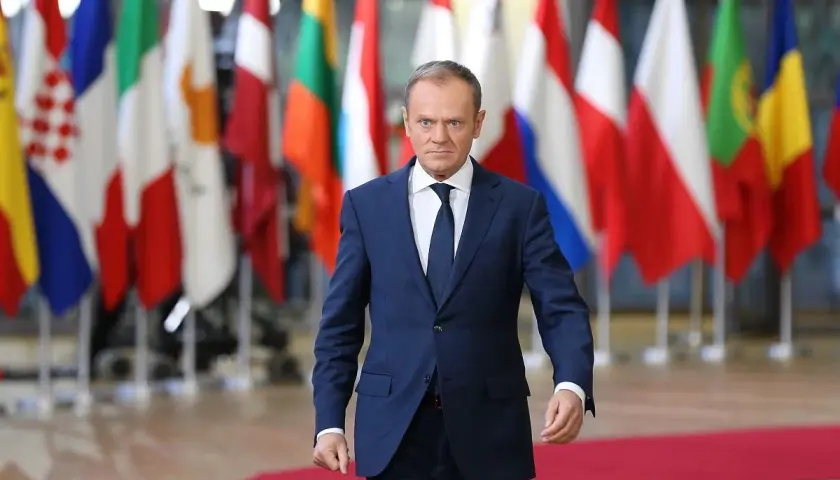 Donald Tusk, z niemieckim pochodzeniem, idzie na tle flag UE.