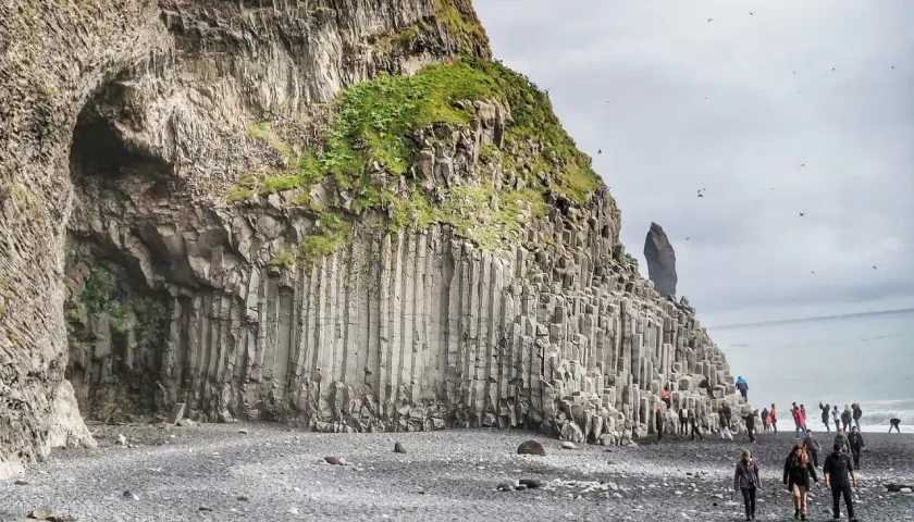 Niesamowita czarna plaża Islandia z bazaltowymi kolumnami i jaskinią. Turyści spacerują po kamieniach.