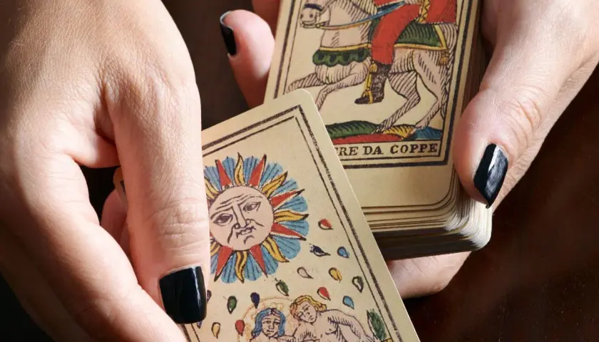 Dłonie trzymają karty tarota, w tym Słońce i rycerza na koniu. Sprawdź, czy tarot online, który się sprawdza, pomoże Ci odkryć przyszłość.