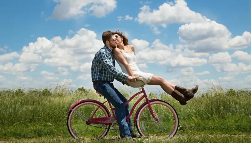 Coppia su bici rosa, lei seduta davanti a lui, baci appassionati sotto un cielo azzurro. Ecco perchè ci si innamora.