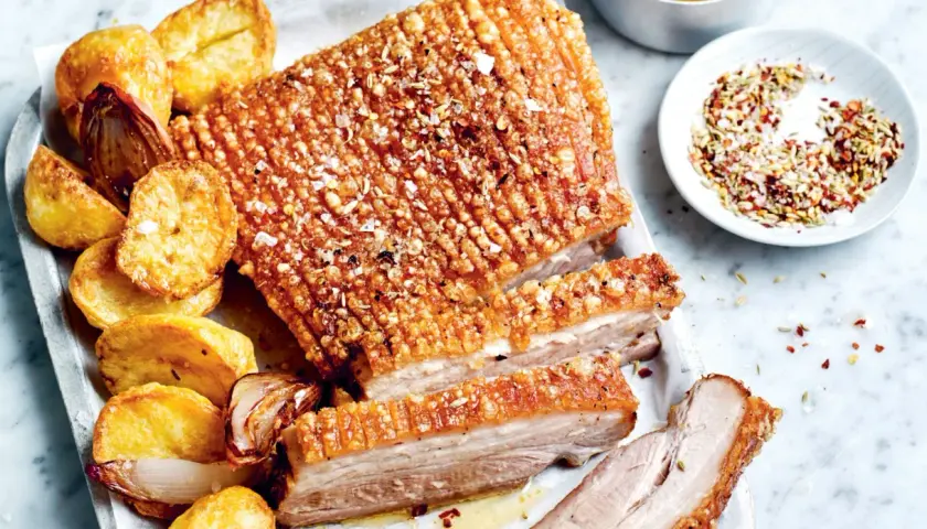 Poitrine de porc croustillante, servie avec des pommes de terre rôties et des oignons caramélisés. Un délice pour les papilles !