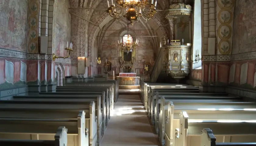 Interiör av en kyrka med bänkar, altare och en predikstol. Väggmålningar och en stor ljuskrona skapar en historisk atmosfär. En av många vackra kyrkor i Stockholm.