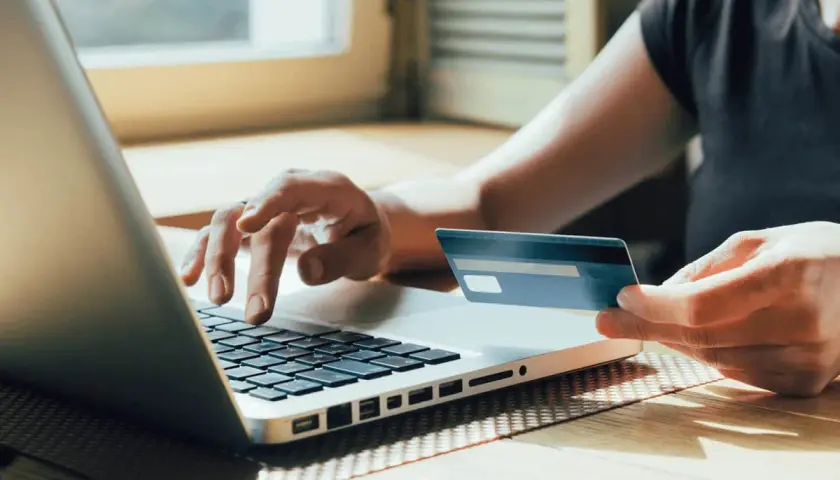 Person tippt auf Laptop, hält Visa-Karte. Prüft auf unberechtigte Abbuchung.