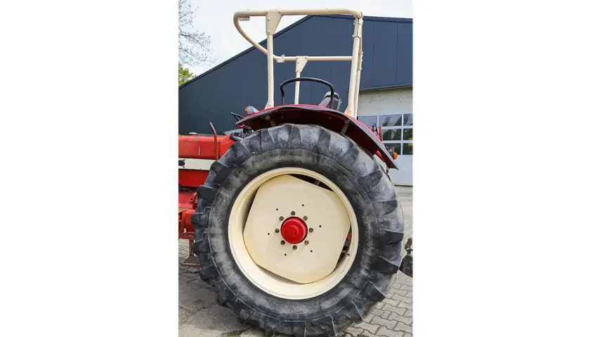 Roter Traktor mit großem Reifen und hellem Felgenhorn. Ein H-Kennzeichen ist am Traktor angebracht.