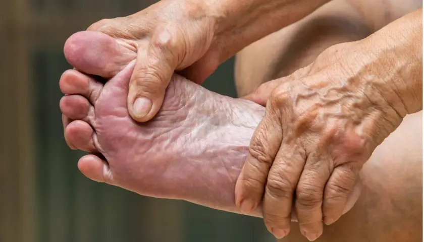 Manos arrugadas masajean un pie, aliviando el dolor de pies.