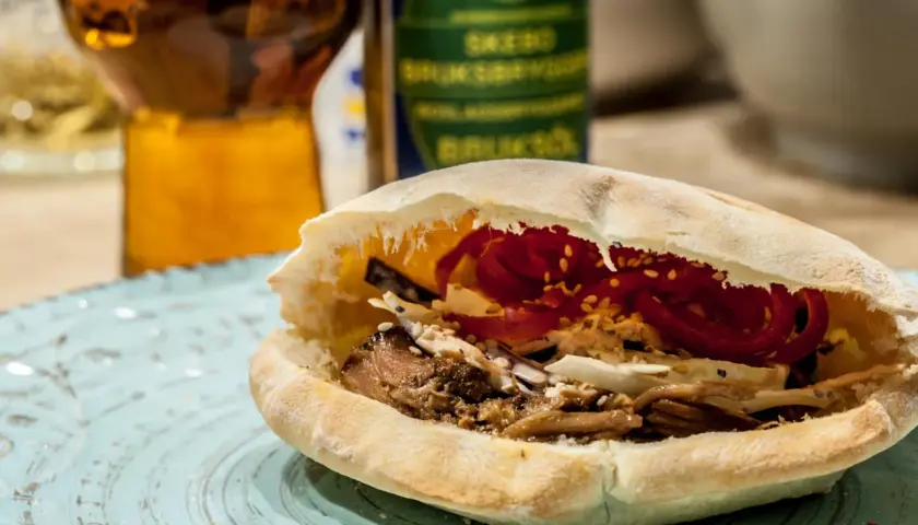 En saftig pulled pork karre-macka i pitabröd, fylld med krispig kål och rödlök. En öl i bakgrunden.