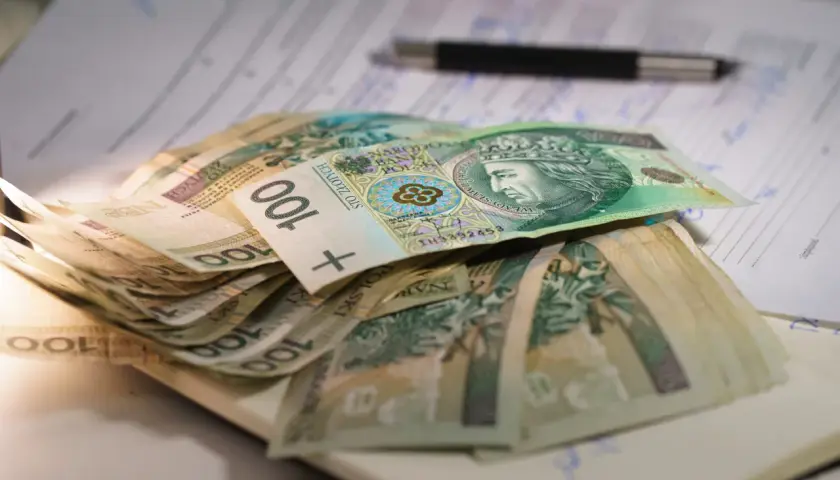Stos banknotów 100 zł leży na dokumentach. Może to być związane z oceną stopnie niepełnosprawności i przyznawanymi świadczeniami.