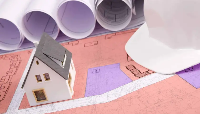 Model domu na planach, biały kask budowlany i zwoje projektów. Planowanie inwestycji, uwzględniające służebność przesyłu.