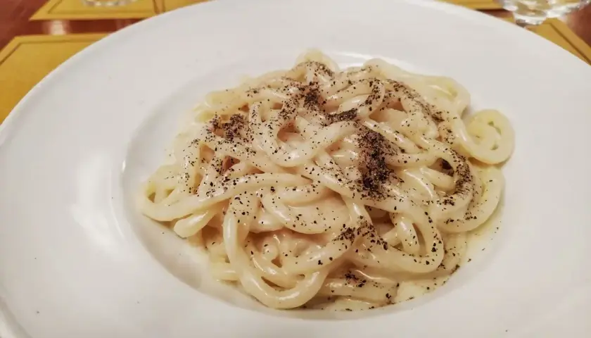 Piatto di pici cacio e pepe, pasta fatta a mano condita con pecorino romano e pepe nero macinato fresco.