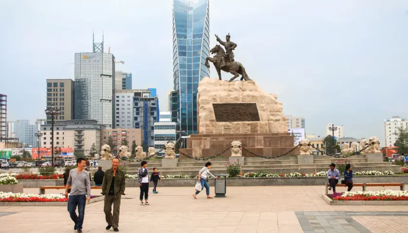Pomnik Czyngis-chana na placu w Ułan Bator, stolicy Mongolii, z nowoczesnymi wieżowcami w tle.