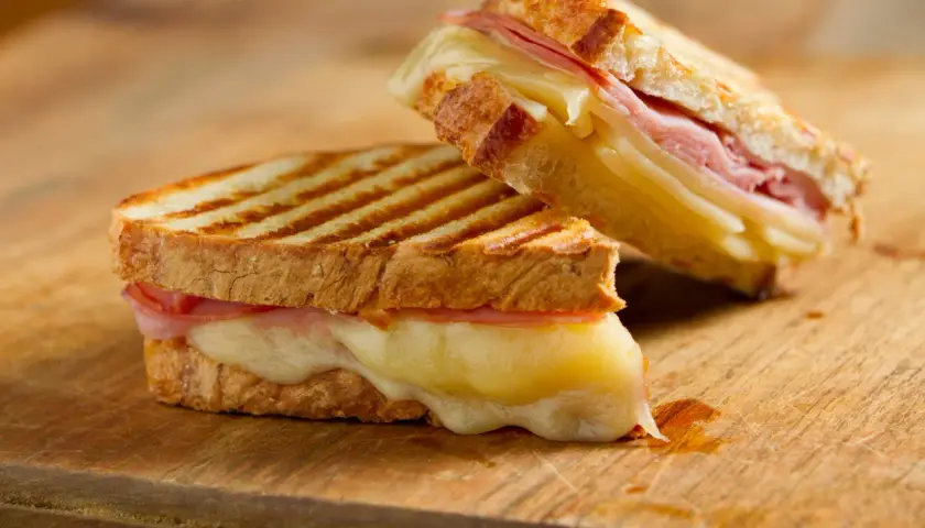 Dos deliciosos panini de queso con jamón, el queso derretido se desborda.