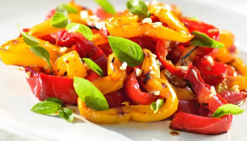 Peperoni al forno colorati, dolci e succosi, guarniti con basilico fresco e aglio. Un contorno estivo perfetto.