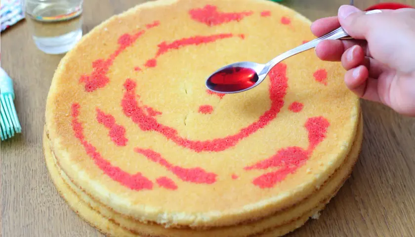 Un cucchiaino di sciroppo rosso viene versato su un pan di spagna a strati, creando un disegno.
