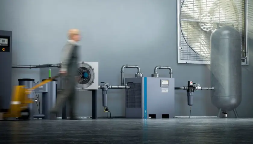 Industrielle Anlage mit Kompressor, Trockner und Luftbehälter. Ein Mitarbeiter mit Hubwagen im Vordergrund. Regelmäßiges kompressor wasser ablassen ist wichtig für die Effizienz.