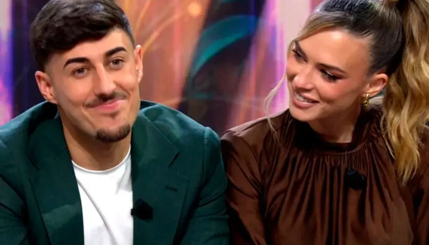 Almudena y Borja, sonriendo y mirando hacia un lado. Él lleva una chaqueta verde y ella un vestido marrón.
