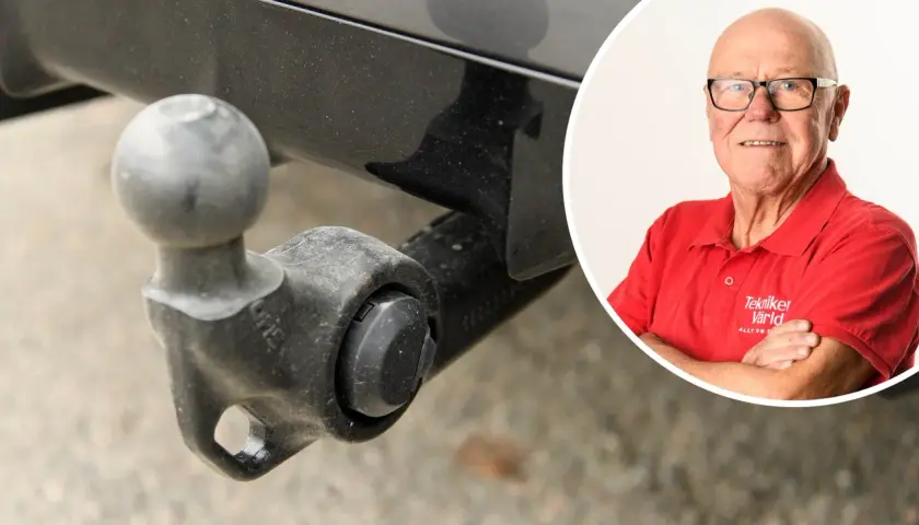En man i röd tröja med texten "Tekniker Värld" ler. Bredvid syns en dragkrok, kanske för en besiktning.