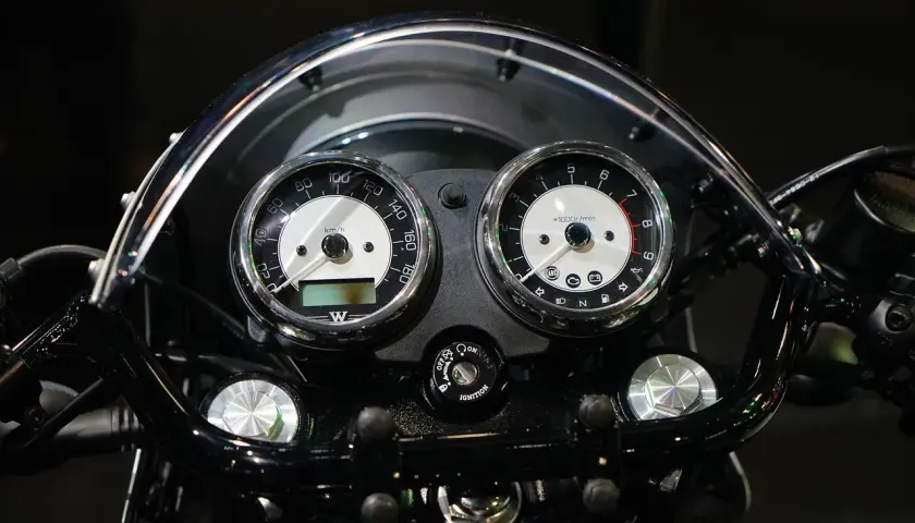Klasyczny przebieg motocykla: prędkościomierz i obrotomierz w chromowanych obudowach, podświetlane kontrolki i kluczyk zapłonu.