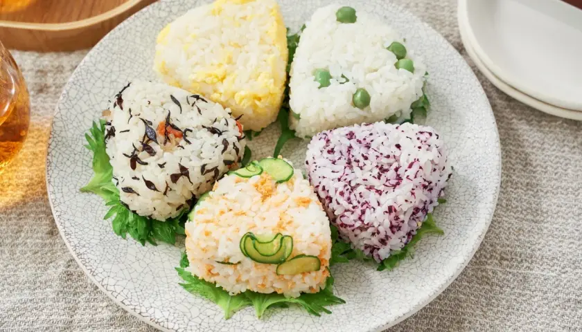 A colorful assortment of musubi vs onigiri, each a unique rice ball shape with various toppings like peas, seaweed, and cucumber.