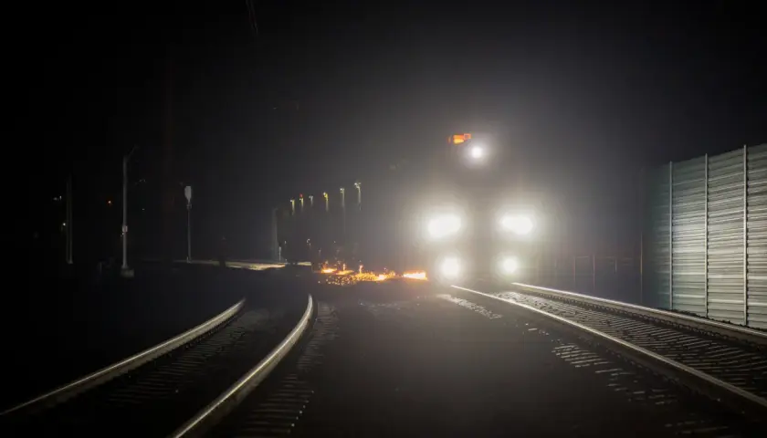 Nocny tor kolejowy rozświetlony reflektorami pociągu i iskrami z prac na torach.