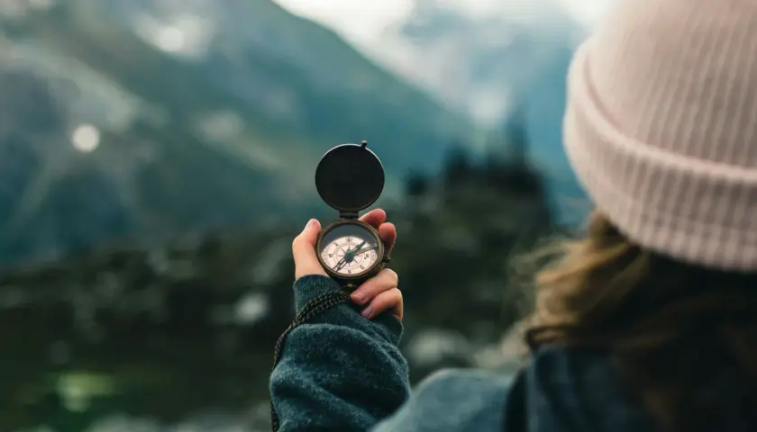 A person in a pink beanie holds a compass, navigating a misty mountain landscape. This symbolizes the journey of transition coaching.