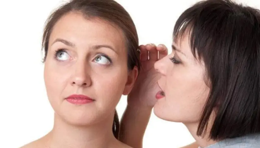 Two women, one whispering into the other's ear.