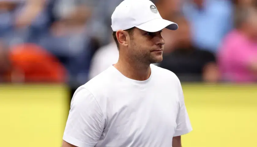 Andy Roddick w białej czapce z logo US Open i białej koszulce, zapatrzony w dal.