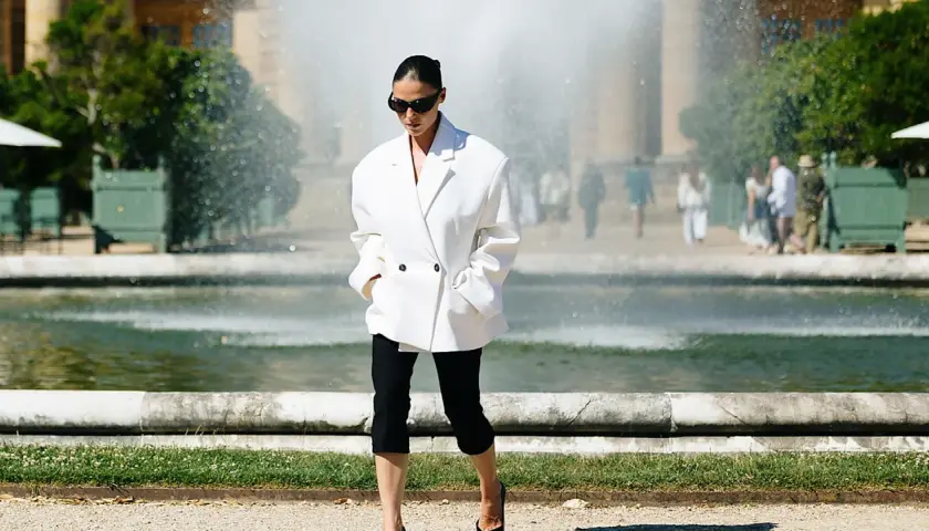 Mujer con un elegante outfit con leggins negro y blazer blanco, paseando cerca de una fuente.