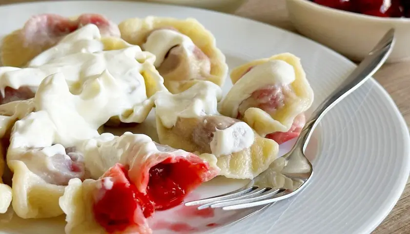 Pyszne pierogi z wiśniami, polane gęstą śmietaną, kuszą soczystym nadzieniem. Idealne na deser lub słodki obiad.