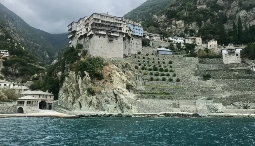 Monastyr na Athos, zbudowany na skalistym zboczu, z tarasowymi ogrodami i widokiem na morze.